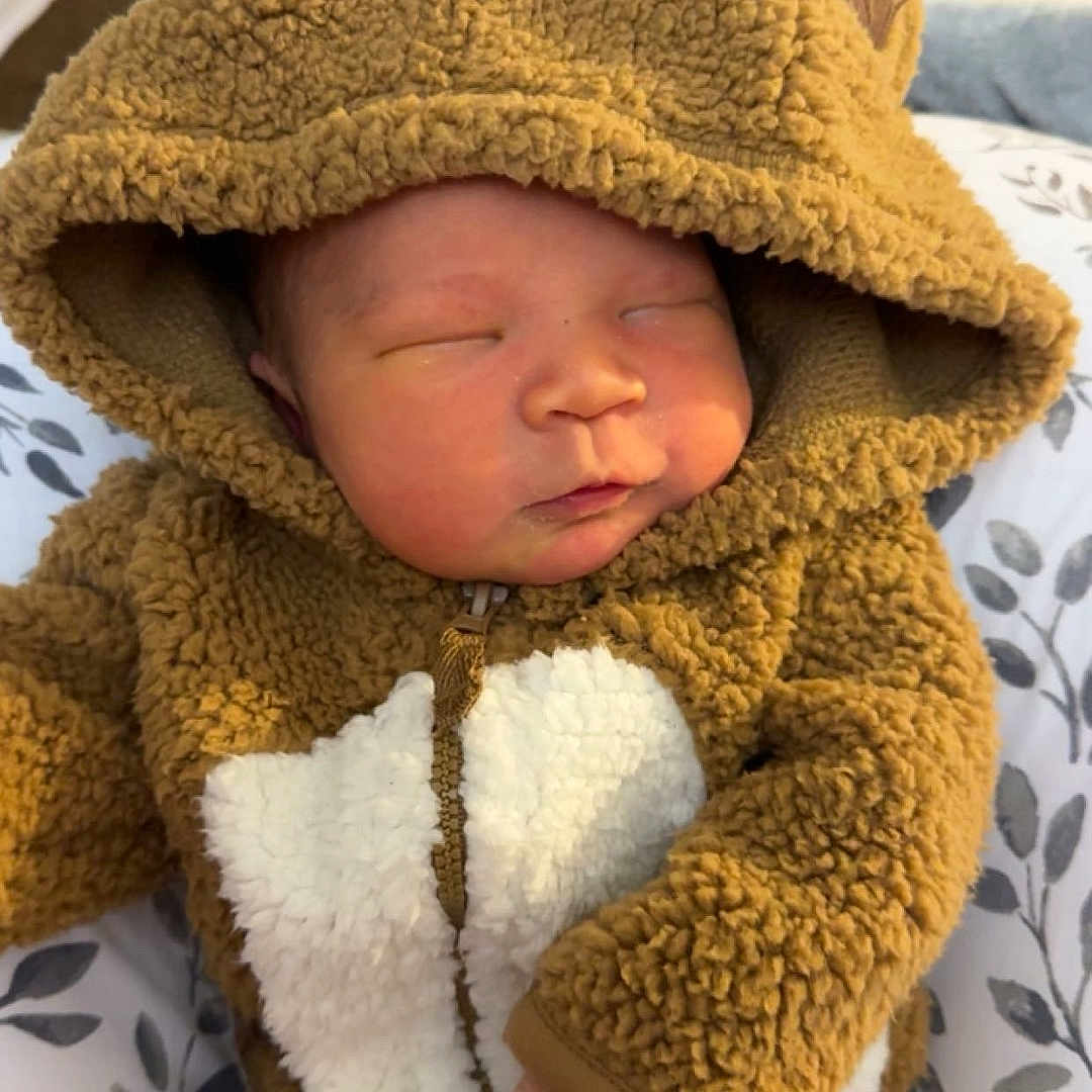 Jenson is registered to the contest to win money with this photo: baby, blanket, bonnet, cap, clothing, coat, face, hat, head, hood, hoodie, jacket, knitwear, newborn, person, photography, portrait, sleeping, sweater, sweatshirt