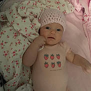 Emory is registered to the contest to win money with this photo: baby, infant, pink_hat, onesie, strawberry_print, blanket, floral_pattern, soft_toys, lying_down, cute, child, indoor, closeup, portrait, clothing, bed, comfort, sleepwear, hand, face