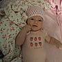 baby, infant, pink_hat, onesie, strawberry_print, blanket, floral_pattern, soft_toys, lying_down, cute, child, indoor, closeup, portrait, clothing, bed, comfort, sleepwear, hand, face
