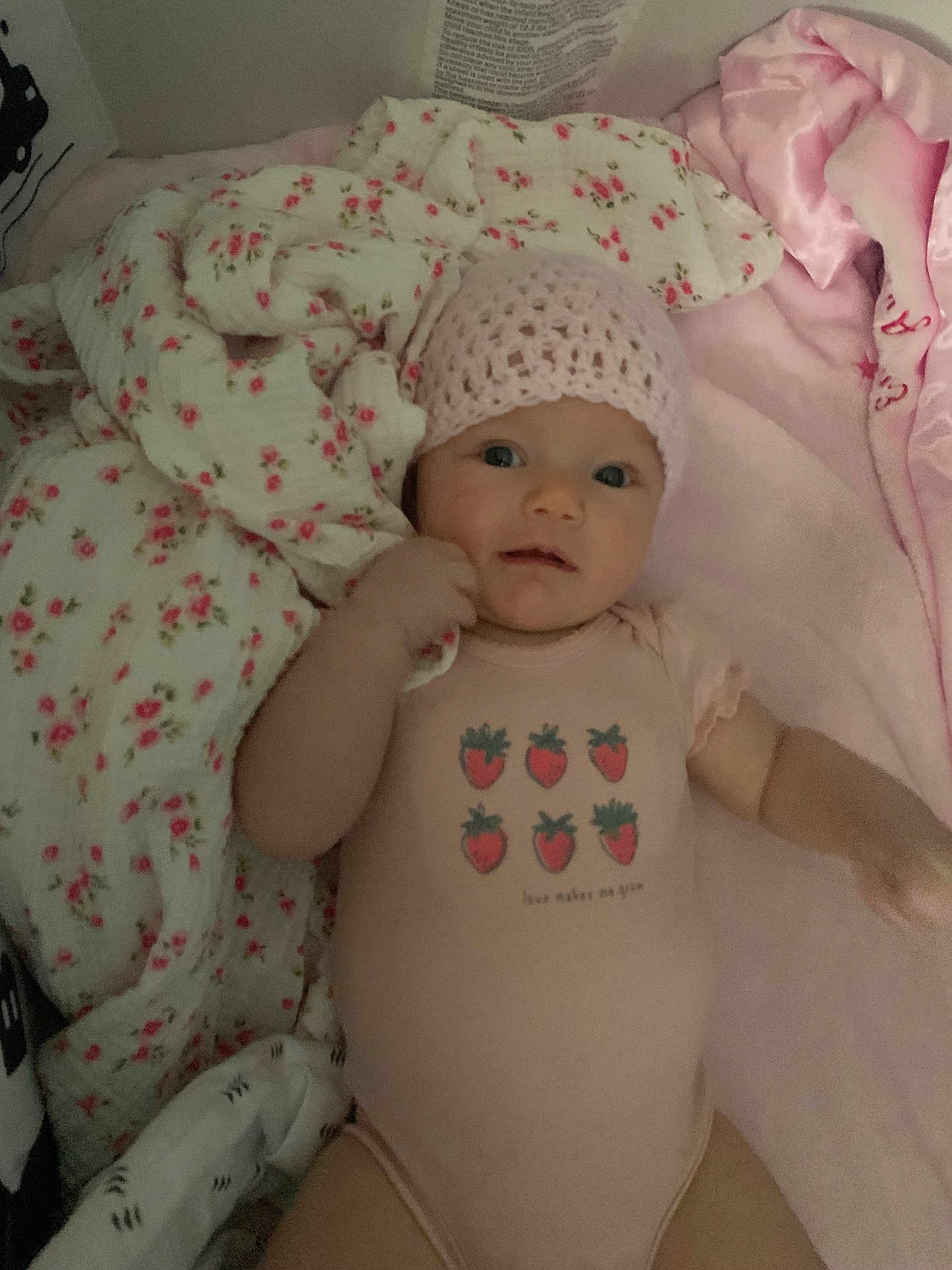 Emory is registered to the contest to win money with this photo: baby, infant, pink_hat, onesie, strawberry_print, blanket, floral_pattern, soft_toys, lying_down, cute, child, indoor, closeup, portrait, clothing, bed, comfort, sleepwear, hand, face