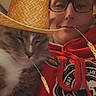 cat, person, portrait, selfie, indoors, hat, straw_hat, glasses, red_clothing, hoodie, gray_cat, white_fur, sleepy, relaxed, close_up, whiskers, face, pet, companionship, humorous