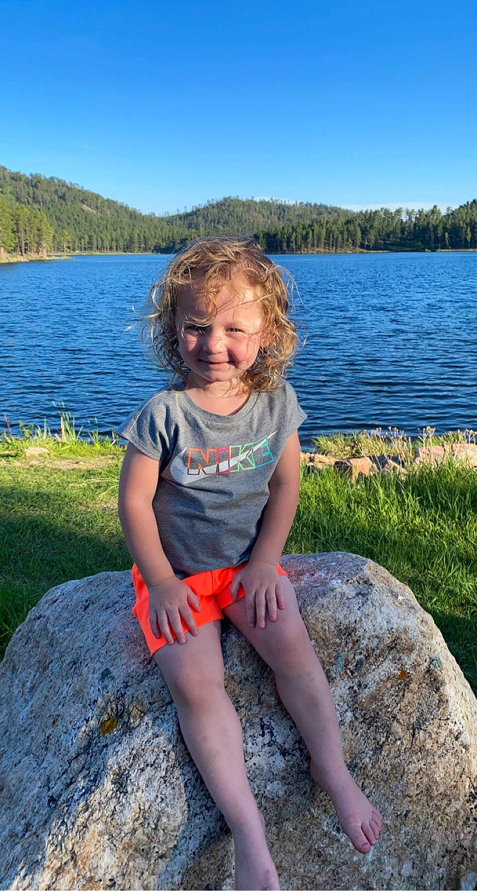Adilynne is registered to the contest to win money with this photo: azure, bank, eye, fun, grass, hair, happy, joy, knee, lake, leaf, leisure, people_in_nature, person, plant, sky, smile, summer, thigh, toddler