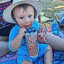 Warren a rejoint le concours — aidez-le/la à gagner de superbes lots ! toddler, child, hat, blue_outfit, cup, outdoor, grass, towel, hand, person, baby_bottle, sunhat, sitting, playful, smiling, cheeky_expression, summer, daylight, family, relaxed