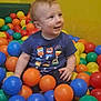 toddler, child, ball_pit, colorful_balls, blue_shirt, smiling, indoor, play_area, yellow_wall, happy, sitting, short_hair, casual_clothing, cute, fun, playful, person, young_child, toy, plastic_balls