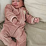 baby, infant, pink_onesie, smile, pillow, blanket, bed, sleepwear, cozy, home, child, cute, newborn, soft_fabric, relaxing, person, indoor, resting, small_hands, face