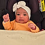 baby, infant, car_seat, headband, blanket, orange_clothing, face, person, child, indoors, cute, newborn, fist, seatbelt, soft_texture, portrait, small_hands, curious, resting, cozy