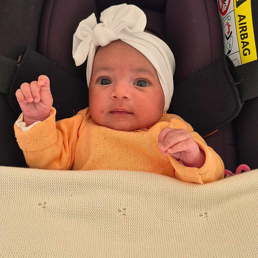 Lyianna participe au concours pour gagner de l'argent avec cette photo : baby, blanket, car_seat, child, cozy, curious, cute, face, fist, headband, indoors, infant, newborn, orange_clothing, person, portrait, resting, seatbelt, small_hands, soft_texture