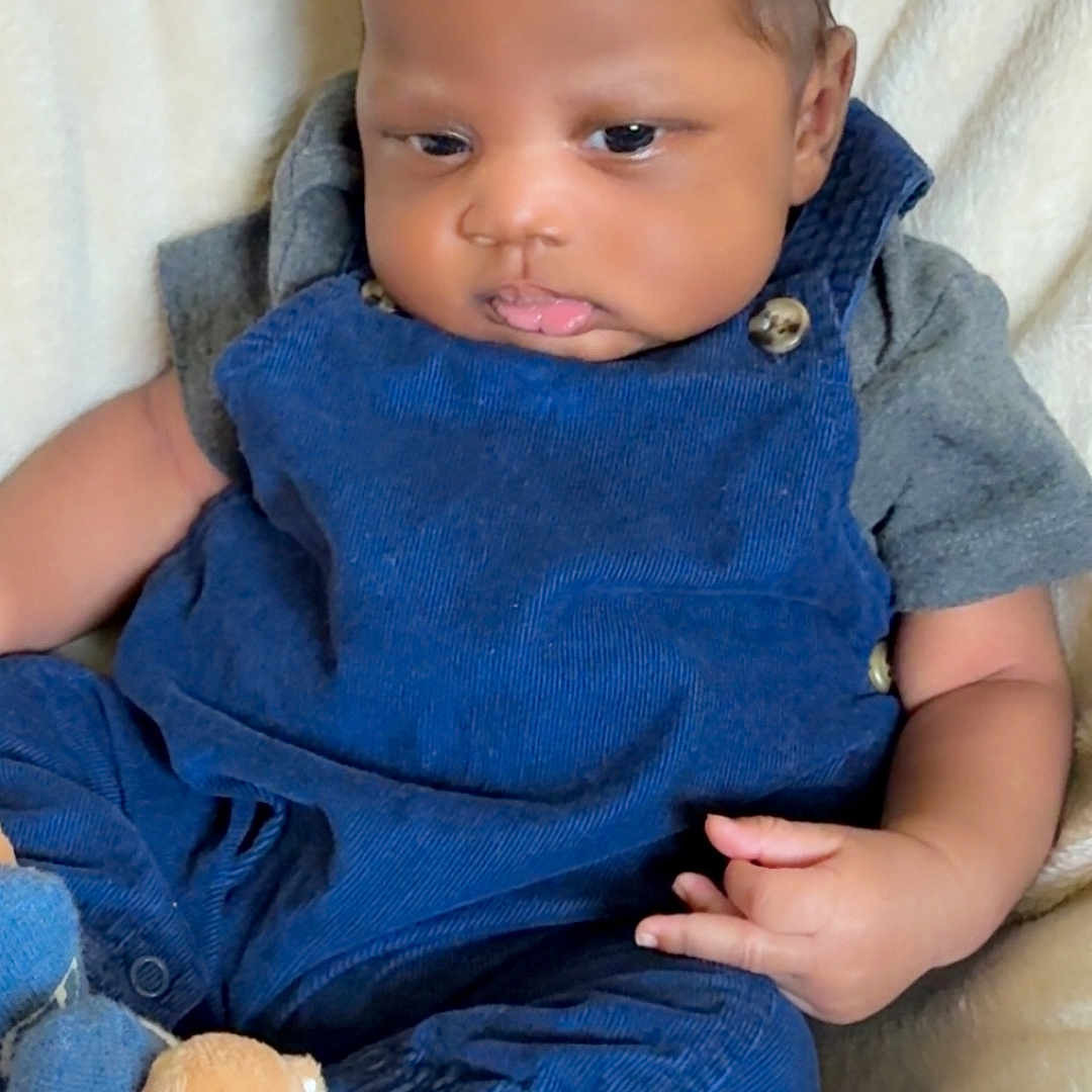 Federrell is registered to the contest to win money with this photo: baby, bear_design, blanket, blue_overalls, casual, child, clothing, comfortable, cozy, curly_hair, cute, indoor, infant, portrait, pouty_face, resting, seated, small_hands, socks, soft_texture