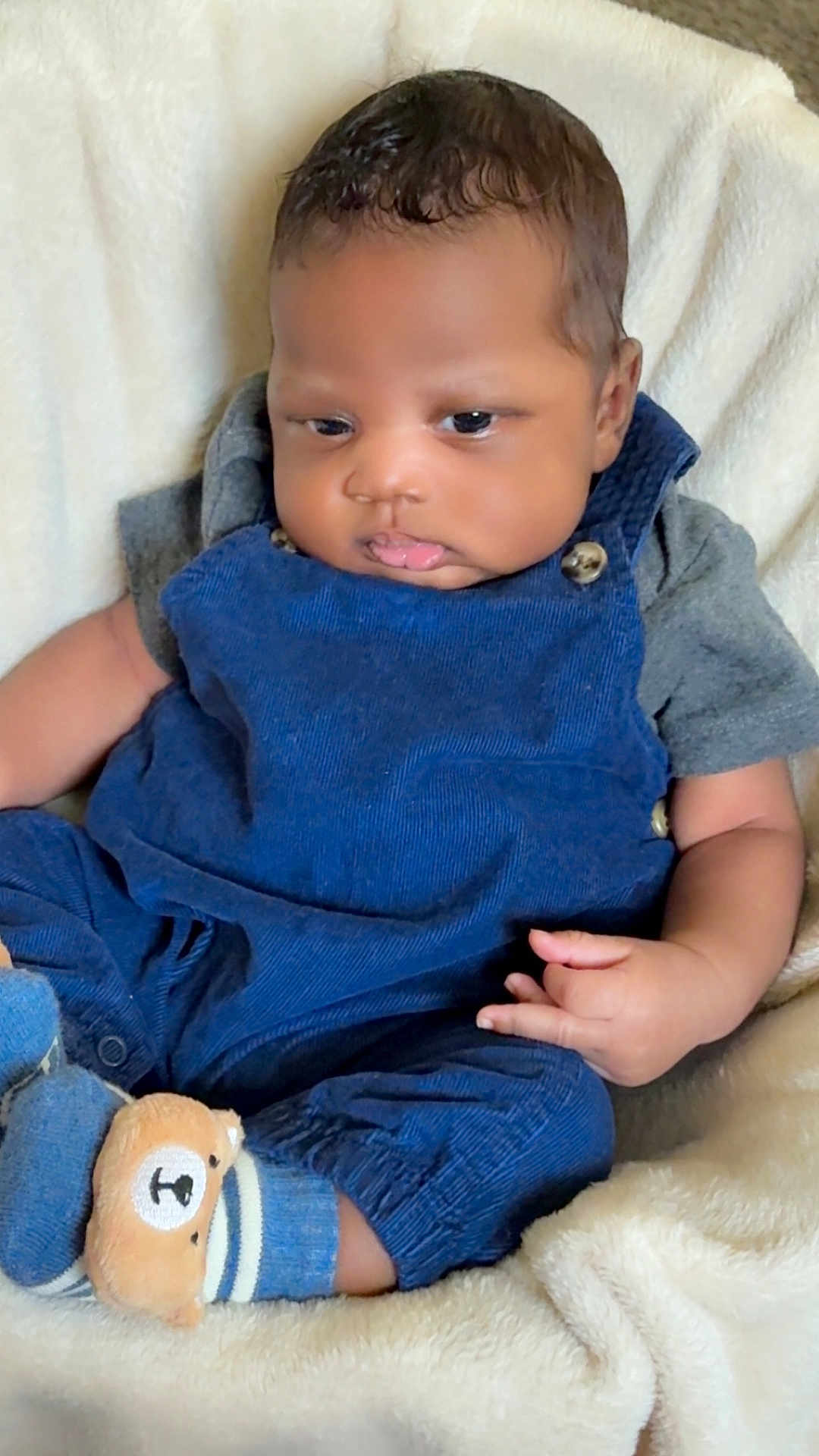 Federrell is registered to the contest to win money with this photo: baby, infant, child, blue_overalls, socks, bear_design, blanket, soft_texture, pouty_face, curly_hair, cute, indoor, comfortable, seated, small_hands, portrait, cozy, clothing, casual, resting