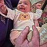 Kateri is registered to the contest to win money with this photo: baby, infant, child, smiling, portrait, indoor, home, onesie, white_clothing, cartoon, cookie_design, raised_arms, hands, adult, holding, rug, carpet, furniture, close_up, happy