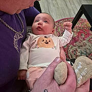 Kateri is registered to the contest to win money with this photo: baby, infant, child, adult, face, portrait, wide_eyes, fist, smiling, clothing, onesie, pumpkin_design, pink_outfit, plush_toy, rug, indoor, home, sitting, close_up, family
