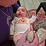 baby, infant, child, adult, face, portrait, wide_eyes, fist, smiling, clothing, onesie, pumpkin_design, pink_outfit, plush_toy, rug, indoor, home, sitting, close_up, family