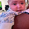 Kateri is registered to the contest to win money with this photo: baby, infant, child, portrait, face, wide_eyed, indoors, sitting, being_held, adult, arm, floral_clothing, blanket, clothing, home, wall_decor, furniture, photography, closeup, adorable