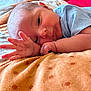 baby, newborn, infant, hand, face, blanket, polka_dots, blue_clothing, lying_down, close_up, skin, cute, soft, peaceful, indoors, resting, portrait, child, sleepy, warm_light