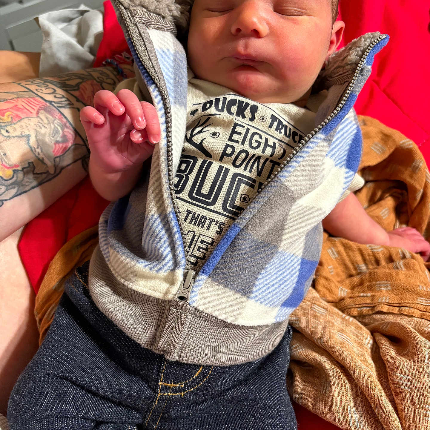 Waylon is registered to the contest to win money with this photo: baby, blanket, closeup, clothing, cozy, cute, fabric, hand, indoor, infant, jeans, newborn, person, resting, skin, sleeping, soft, tattoo, vest, warm