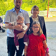 Mario Cros a rejoint le concours — aidez-le/la à gagner de superbes lots ! baby, casual_clothing, child, family, glasses, greenery, group, happy, holding, man, nature, outdoor, people, picket_fence, portrait, red_dress, ribbons, smile, sunlight, woman
