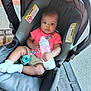 baby, bottle, car_seat, child, clothing, coral_shirt, floor, footwear, infant, pacifier, person, plastic_bottle, socks, seat, seatbelt, sidewalk, sitting, skin, toy, young_child
