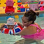 baby, child, woman, swimming_pool, swim_ring, floatation_device, pink_swimsuit, glasses, peppa_pig, toys, indoor_pool, water, smiling, playful, colorful, safety, fun, family, parent, recreation