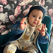 Adem a rejoint le concours — aidez-le/la à gagner de superbes lots ! baby, beanie, child, chubby_cheeks, cute, denim_jacket, dinosaur_pajamas, eyes, face, floral_wallpaper, hands, hat, indoors, infant, patterned_background, playful_expression, portrait, sitting, sock, teal_chair