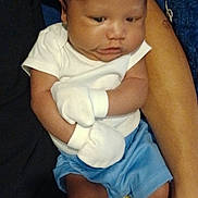 Josiah is registered to the contest to win money with this photo: baby, infant, mittens, white_shirt, blue_shorts, socks, arm, person, resting, indoor, skin, cute, child, holding, casual_clothing, portrait, newborn, young, comfort, family