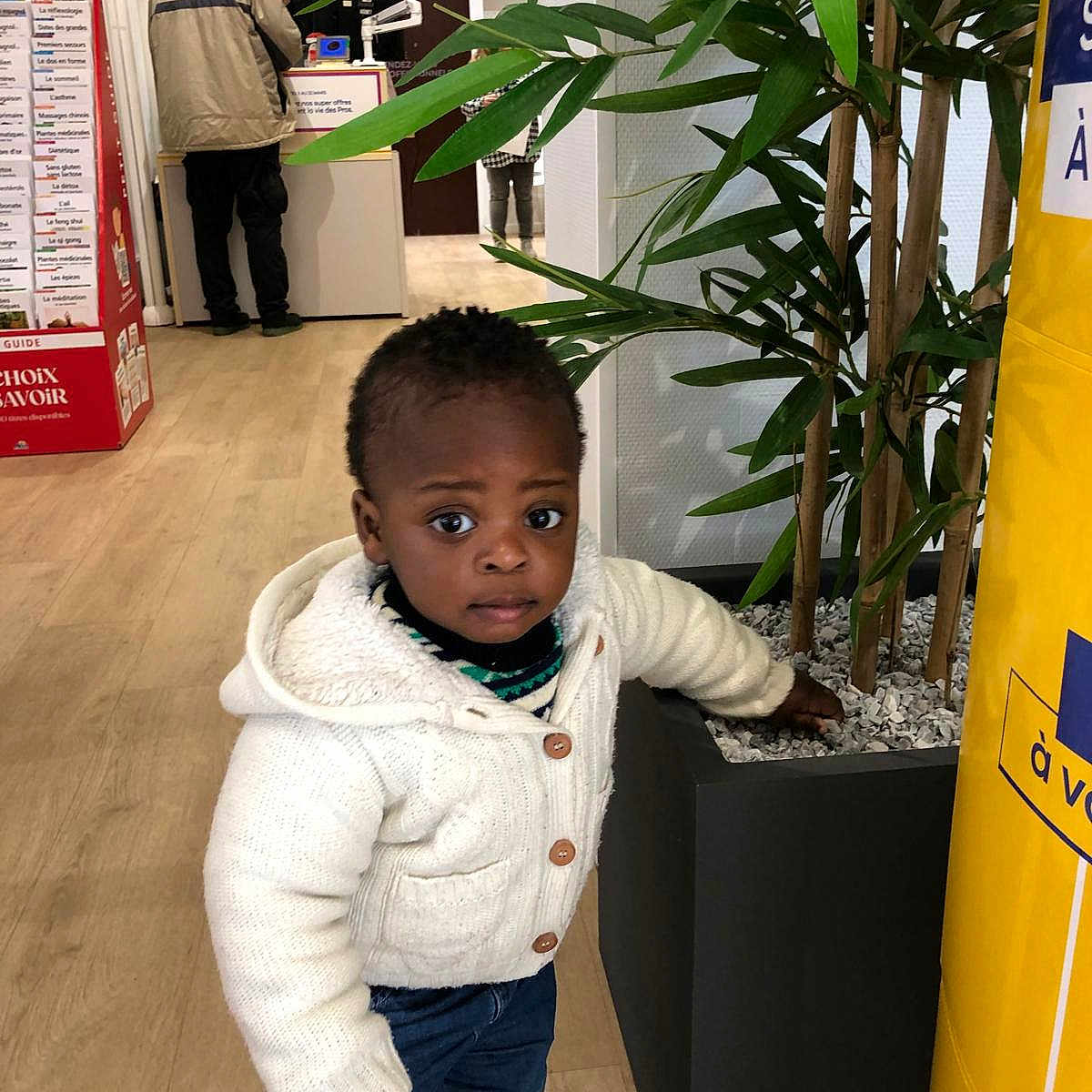 Yerim a rejoint le concours — aidez-le/la à gagner de superbes lots ! adult, casual_clothing, child, conversation, curious, exploration, expression, floor, green, indoor, jeans, leaf, people, plant, portrait, pot, standing, sweater, toddler, wooden_floor