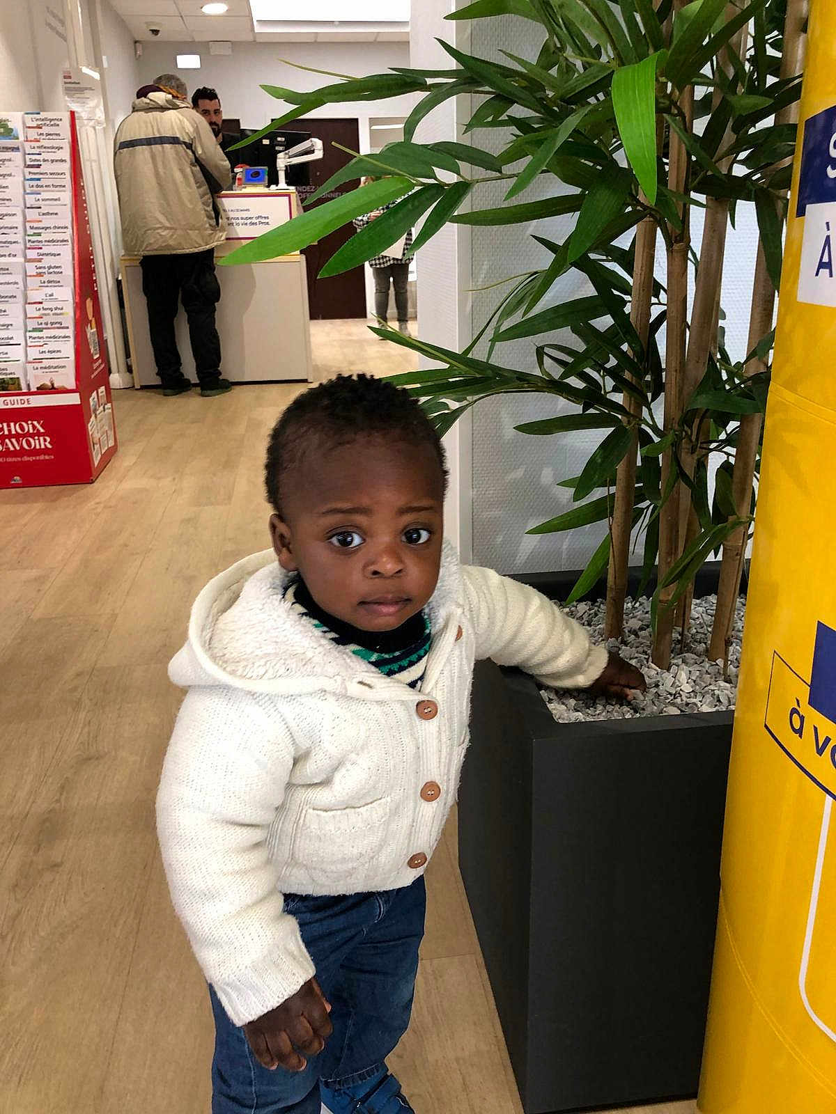 Yerim a rejoint le concours — aidez-le/la à gagner de superbes lots ! toddler, child, indoor, plant, pot, sweater, jeans, curious, exploration, people, floor, wooden_floor, leaf, green, adult, conversation, casual_clothing, standing, expression, portrait