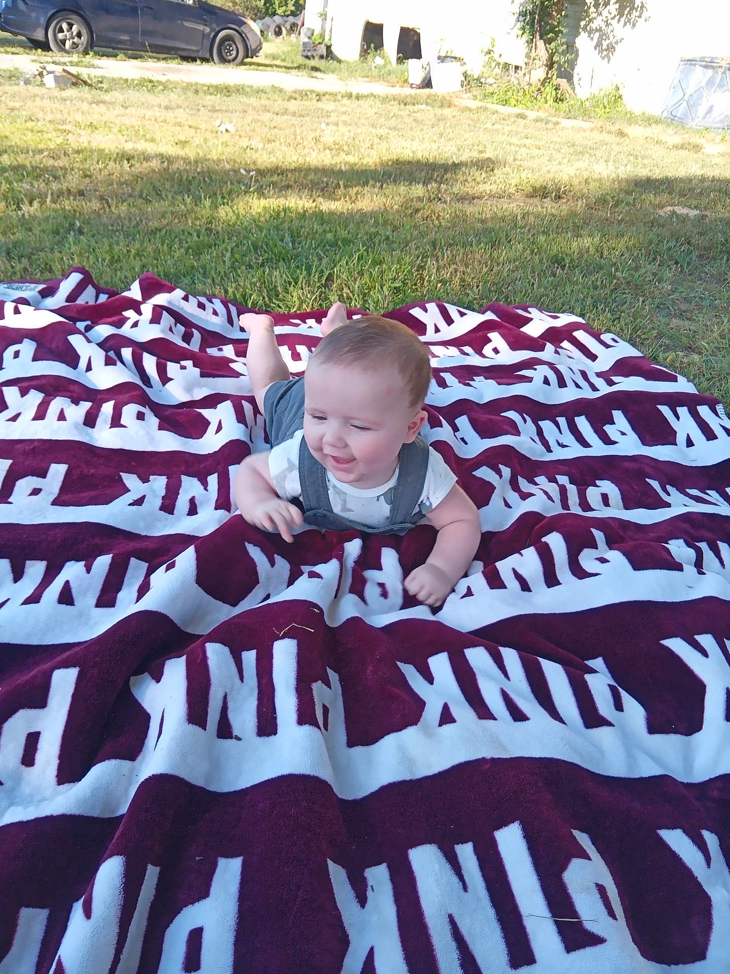 Karson joined the competition — help win amazing prizes! baby, child, blanket, outdoor, grass, sunlight, smiling, happy, person, car, vehicle, nature, greenery, clothing, head, face, playing, summer, relaxing, yard