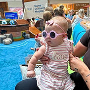 Sophia joined the competition — help win amazing prizes! baby, child, indoor, play_area, sunglasses, pink_clothing, striped_clothing, adult_hand, pirate_ship, blue_carpet, hospital_sign, people, woman, tattoo, headband, toy, shopping_mall, casual_clothing, cute, childrens_hospital
