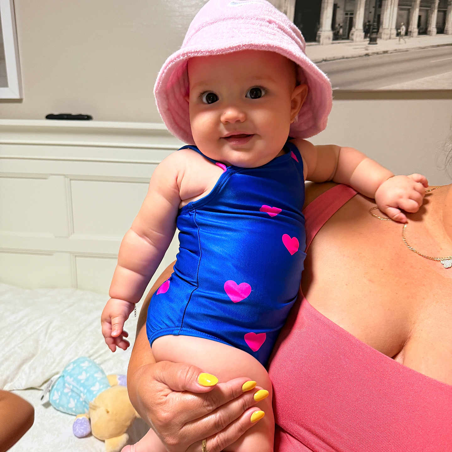 Sophia joined the competition — help win amazing prizes! adult_hand, baby, bed, blue_swimsuit, child, cute, fingers, hearts, holding, indoor, jewelry, nail_polish, person, pink_hat, plush_toy, portrait, room, skin, smiling, yellow_nails