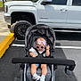 Sophia is registered to the contest to win money with this photo: baby, stroller, pink_bow, sunglasses, hand_gesture, white_truck, parking_lot, asphalt, yellow_curb, gray_stroller, child, casual_clothing, footwear, outdoor, daylight, sidewalk, vehicle, wheel, shoes, baby_accessories