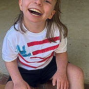 Anna is registered to the contest to win money with this photo: child, smiling, happy, sitting, doorstep, white_tshirt, bows, red_bow, blue_bow, shorts, brick_wall, door, porch, casual_clothing, outdoor, person, young_child, portrait, daylight, concrete_floor