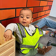 Gaborrayansamir a rejoint le concours — aidez-le/la à gagner de superbes lots ! toddler, child, safety_vest, yellow, orange_wall, toy, hammer, floor, jeans, slippers, wooden_box, indoor, curious, sitting, playtime, person, clothing, casual, young_child, home