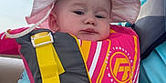 Vivian is registered to the contest to win money with this photo: baby, child, life_jacket, hat, sunhat, safety, outdoor, water_sport, clothing, person, infant, expression, hand, seat, blue_sleeves, yellow_strap, pink, yellow, gray, portrait