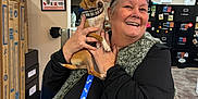 Socks is registered to the contest to win money with this photo: cabinet, cardboard_boxes, chihuahua, collar, dog, floor, fuzzy_vest, happy, holding, indoor, leash, magnet, office, person, pet_store, posters, sitting, smiling, table, woman