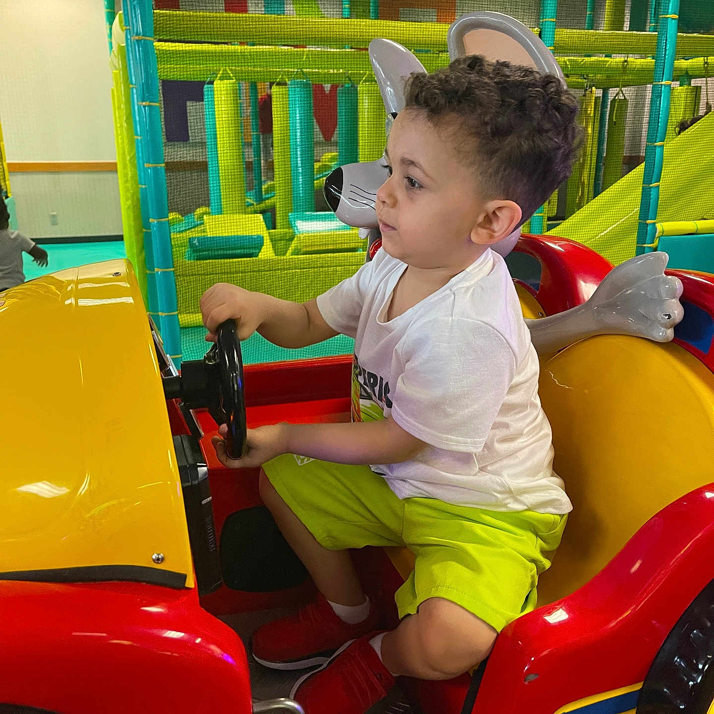 Khaled joined the competition — help win amazing prizes! boy, child, colorful, curly_hair, entertainment, footwear, fun, green, indoor_play_area, kid, kiddie_ride, playground, playing, red, shorts, side_view, steering_wheel, toy_car, tshirt, yellow