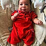baby, infant, red_clothing, plush_toys, baby_seat, indoor, curious_expression, cute, child, legs, hands, patterned_fabric, floor, toy, seat, person, portrait, comfortable, smiling, cute_baby