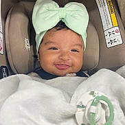 Zipporah is registered to the contest to win money with this photo: baby, infant, car_seat, headband, bow, blanket, pacifier, smile, face, clothing, earrings, child, cute, indoor, portrait, person, baby_accessory, soft, comfort, happy