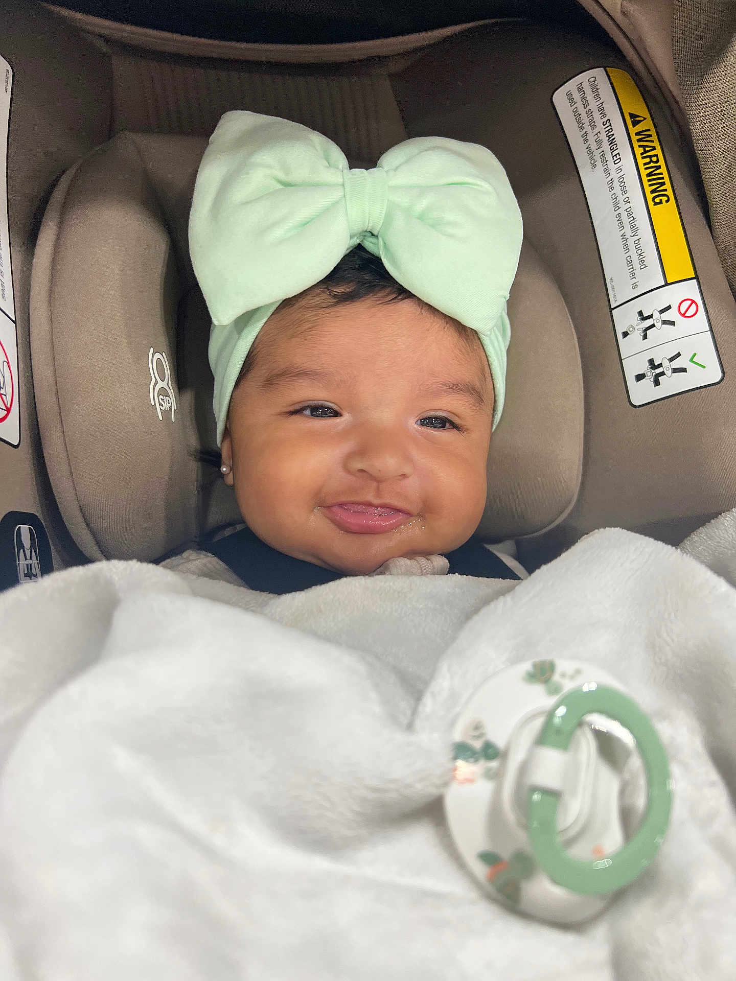 Zipporah is registered to the contest to win money with this photo: baby, infant, car_seat, headband, bow, blanket, pacifier, smile, face, clothing, earrings, child, cute, indoor, portrait, person, baby_accessory, soft, comfort, happy