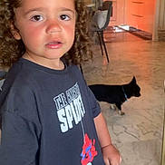 Ilan a rejoint le concours — aidez-le/la à gagner de superbes lots ! child, curly_hair, black_tshirt, spiderman, indoor, marble_floor, dog, black_dog, kitchen, chair, table, person, casual_clothing, young_child, curious_expression, home_interior, flooring, pet, animal, furniture