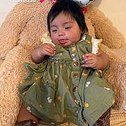 Kennedy is registered to the contest to win money with this photo: baby, child, teddy_bear, dress, boots, brown_boots, green_dress, floral, cute, indoors, plush_toy, sitting, person, face, tongue_out, playful, cozy, text_overlay, heart_emoji, comfort