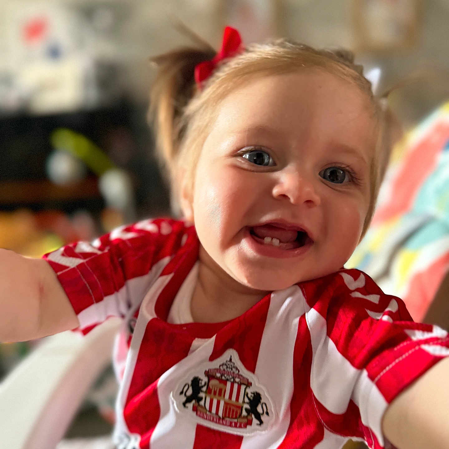 Dakota-Mae is registered to the contest to win money with this photo: baby, blurred_background, cheerful, child, closeup, cute, face, happy, indoor, person, pigtails, playful, portrait, reaching, red_and_white_stripes, red_bow, smiling, sports_jersey, toddler, young_child