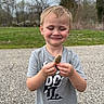 child, boy, smile, mushroom, morel, outdoor, nature, grass, trees, cloudy_sky, gravel_path, casual_clothing, shorts, tshirt, standing, happy, daylight, forest_edge, young, person