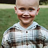 child, boy, smile, face, portrait, plaid_shirt, hoodie, outdoor, green_background, happy, young, cute, casual_clothing, blond_hair, rosy_cheeks, natural_light, person, head_and_shoulders, eyes, friendly