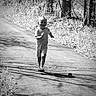 child, toddler, running, outdoor, pathway, black_and_white, smiling, nature, trees, grass, shadow, sunlight, casual_clothing, sandals, happy, person, daytime, playful, portrait, motion