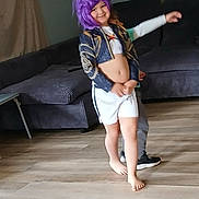 Ella joined the competition — help win amazing prizes! child, purple_wig, smiling, barefoot, shorts, jacket, living_room, sofa, wooden_floor, playful, person, indoor, fun, two_children, curtain, casual_clothing, happy, home, candid, posing