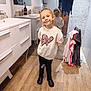child, girl, smiling, bathroom, mirror, reflection, sweatshirt, hearts, leopard_print, black_pants, boots, towels, wood_floor, sink, cabinet, home_interior, standing, happy, casual_clothing, pose