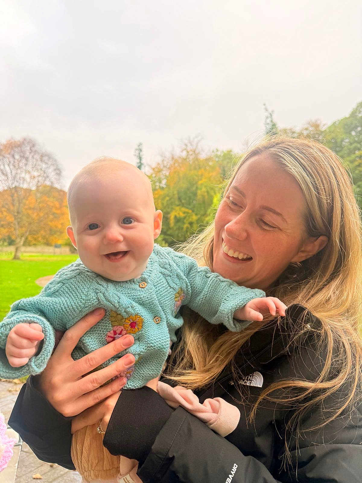 Grace joined the competition — help win amazing prizes! baby, woman, smile, outdoor, autumn, trees, grass, knitted_sweater, floral_embroidery, holding, happy, person, nature, fall, jacket, long_hair, park, daylight, child, family
