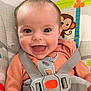 baby, baby_seat, blue_eyes, cheerful, child, child_seat, closeup, cute, elephant_patch, face, happy, indoors, infant, monkey, orange_clothing, playful, safety_harness, seatbelt, smiling, toy_pattern