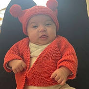 Mïa participe au concours pour gagner de l'argent avec cette photo : baby, infant, knit_hat, pom_poms, cardigan, orange_clothing, booties, onesie, sitting, legs, hands, cheeks, portrait, indoors, curtains, soft_light, cozy, cute, person, photography