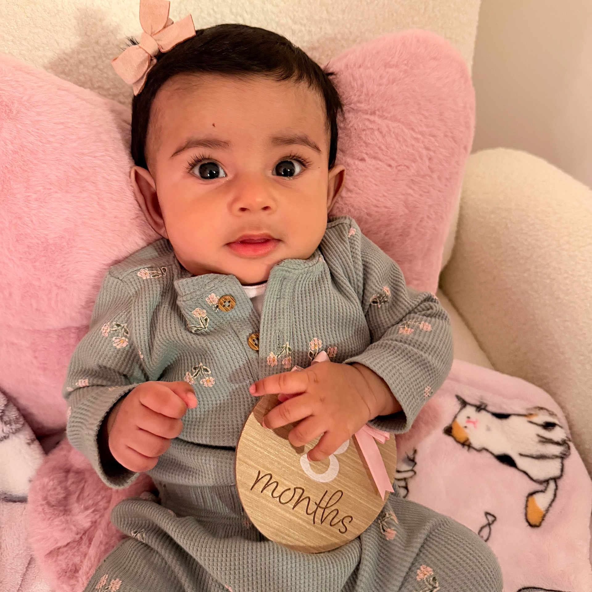 Anaya joined the competition — help win amazing prizes! baby, infant, child, pink_bow, plaque, 8_months, cushion, blanket, cute, portrait, indoors, clothing, long_sleeve, patterned_outfit, hand, face, eyes, sitting, soft_texture, milestone